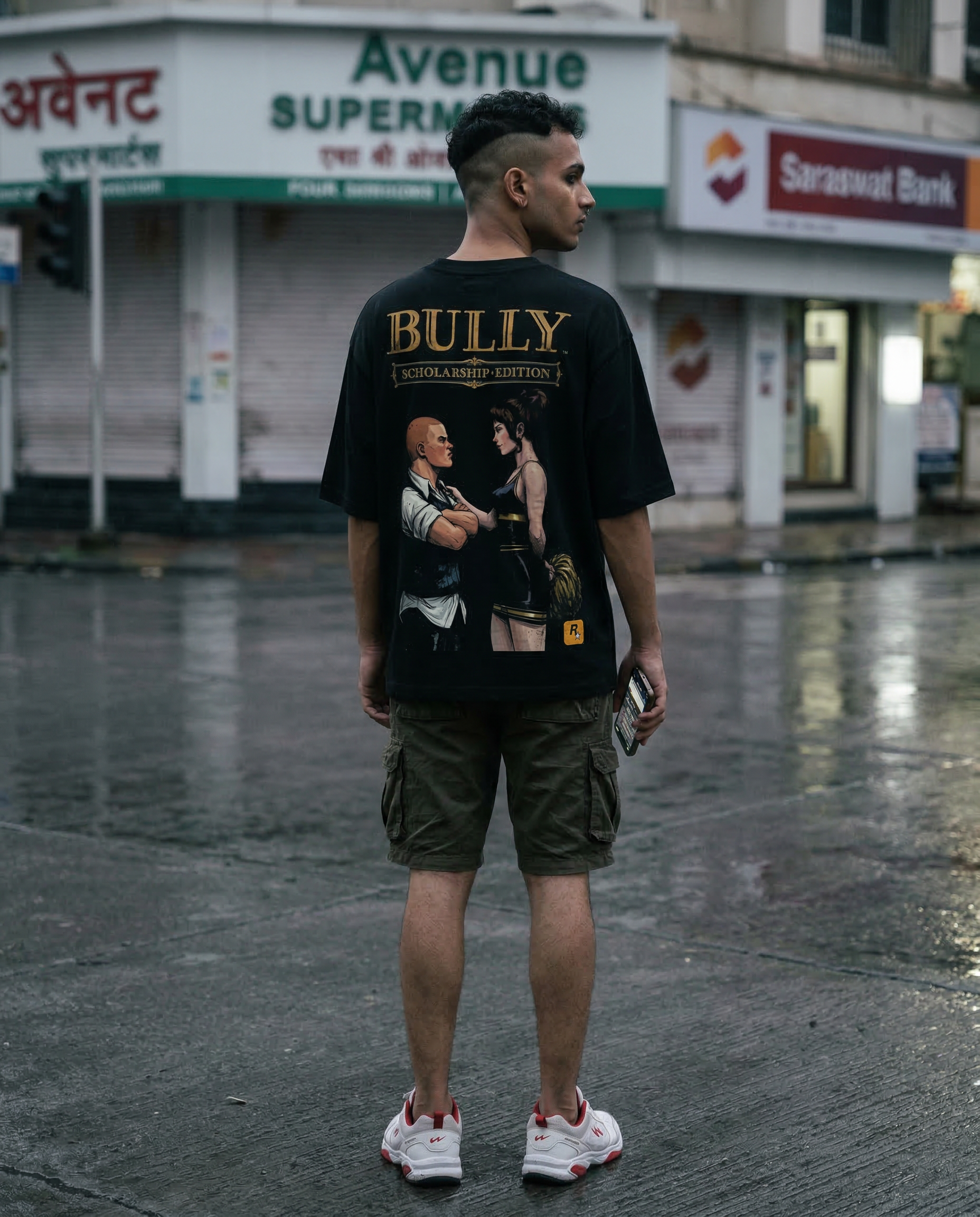 Androgynous Indian youth scrolling at empty junction in rain-grey night, back-turned intimacy of oversized tee and loose limbs.